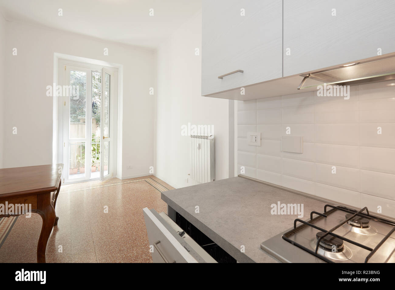 White wooden kitchen with cooker and dishwasher in renovated apartment, sunlight Stock Photo