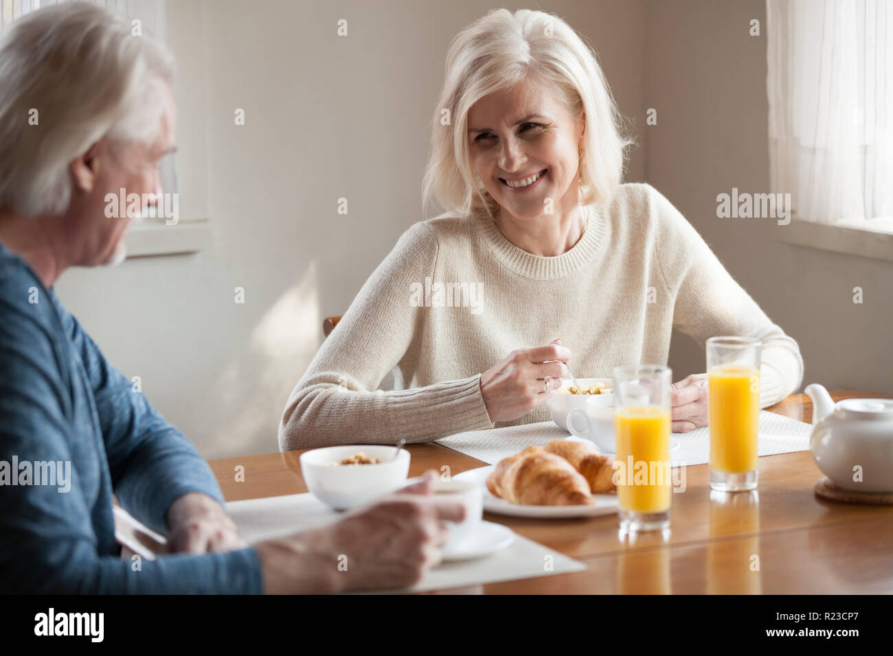 Happy aged husband and wife enjoy breakfast spending time at home together, senior couple eating healthy food smiling talking in morning, laughing eld Stock Photo