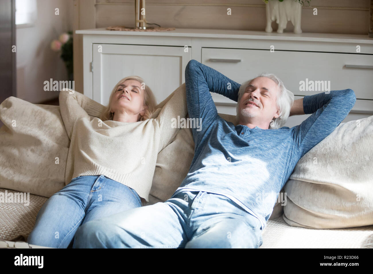 Calm senior husband and wife lying on cozy couch at home relaxing