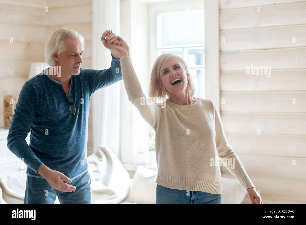 Happy senior husband and wife have fun spending time in country house together, smiling aged couple dance swirling and swaying at home, excited elderl Stock Photo