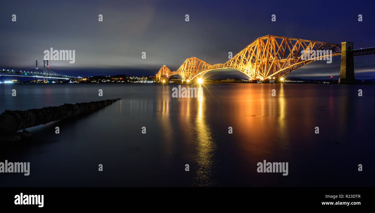 The Forth Bridge is brightly lit at dusk on the Firth of Forth at South Queensferry in Edinburgh, Scotland. Stock Photo