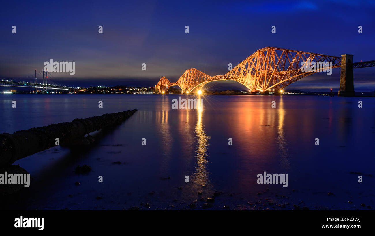 The Forth Bridge is brightly lit at dusk on the Firth of Forth at South Queensferry in Edinburgh, Scotland. Stock Photo