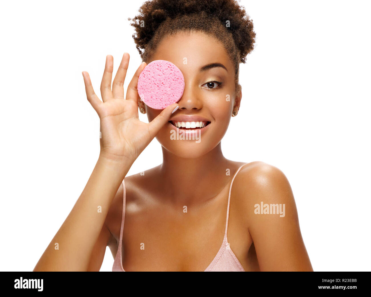 Funny girl holding pink sponge near her face. Portrait of young african american girl on white background. Youth and skin care concept Stock Photo