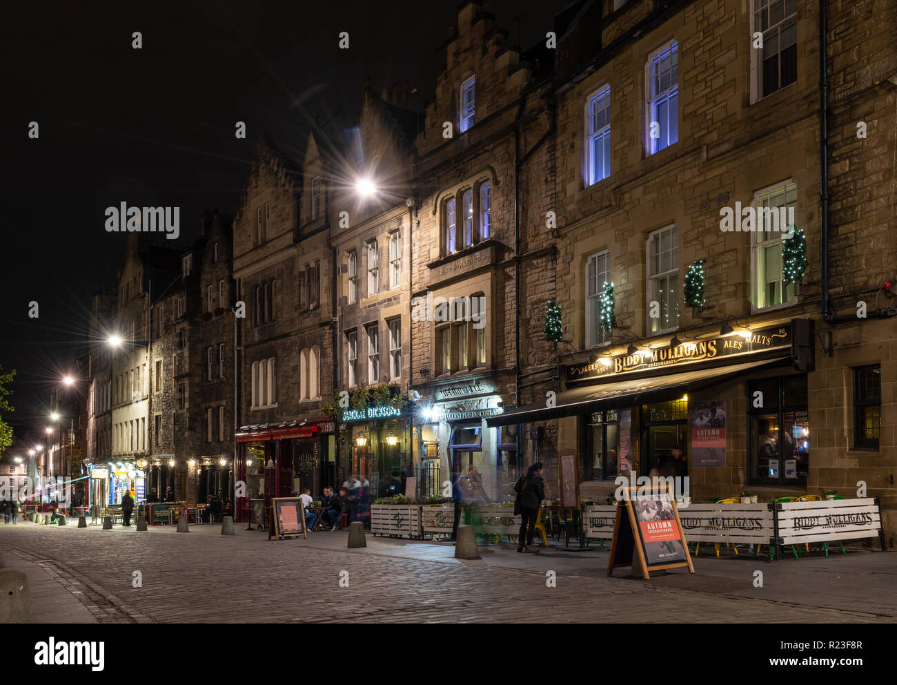 Edinburgh, Scotland, UK - November 2, 2018: Punters drink outside pubs and bars along Edinburgh's traditional cobbled Grassmarket street at night. Stock Photo