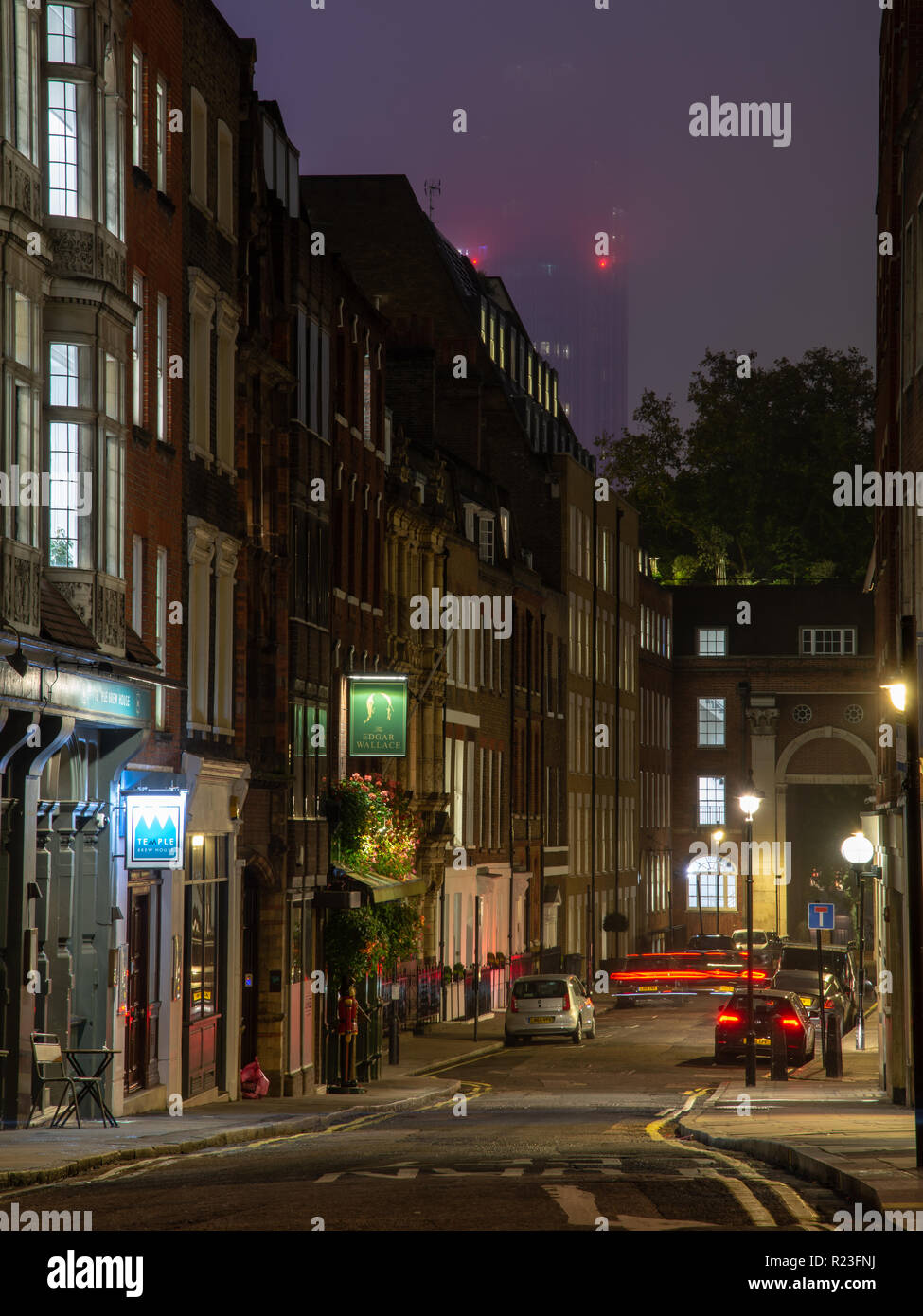 London, England, UK - October 15, 2018: Houses and pubs in London's Temple neighbourhood are lit at night, with a city skyscraper half hidden in mist  Stock Photo