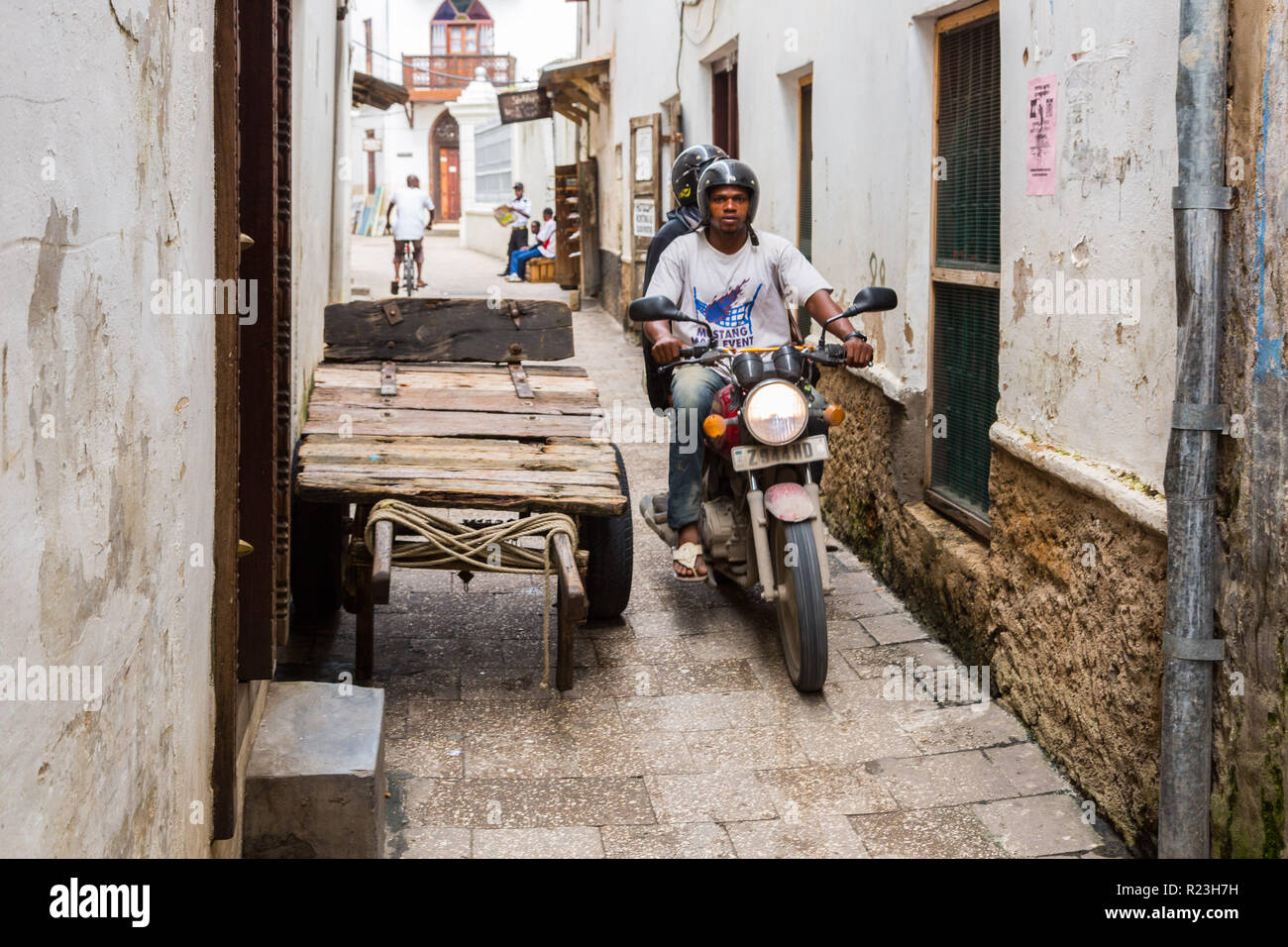 Two local men driving a motorcycle through narrow streets of Stone Town, old colonial center of Zanzibar City, Unguja island, Tanzania. Stock Photo