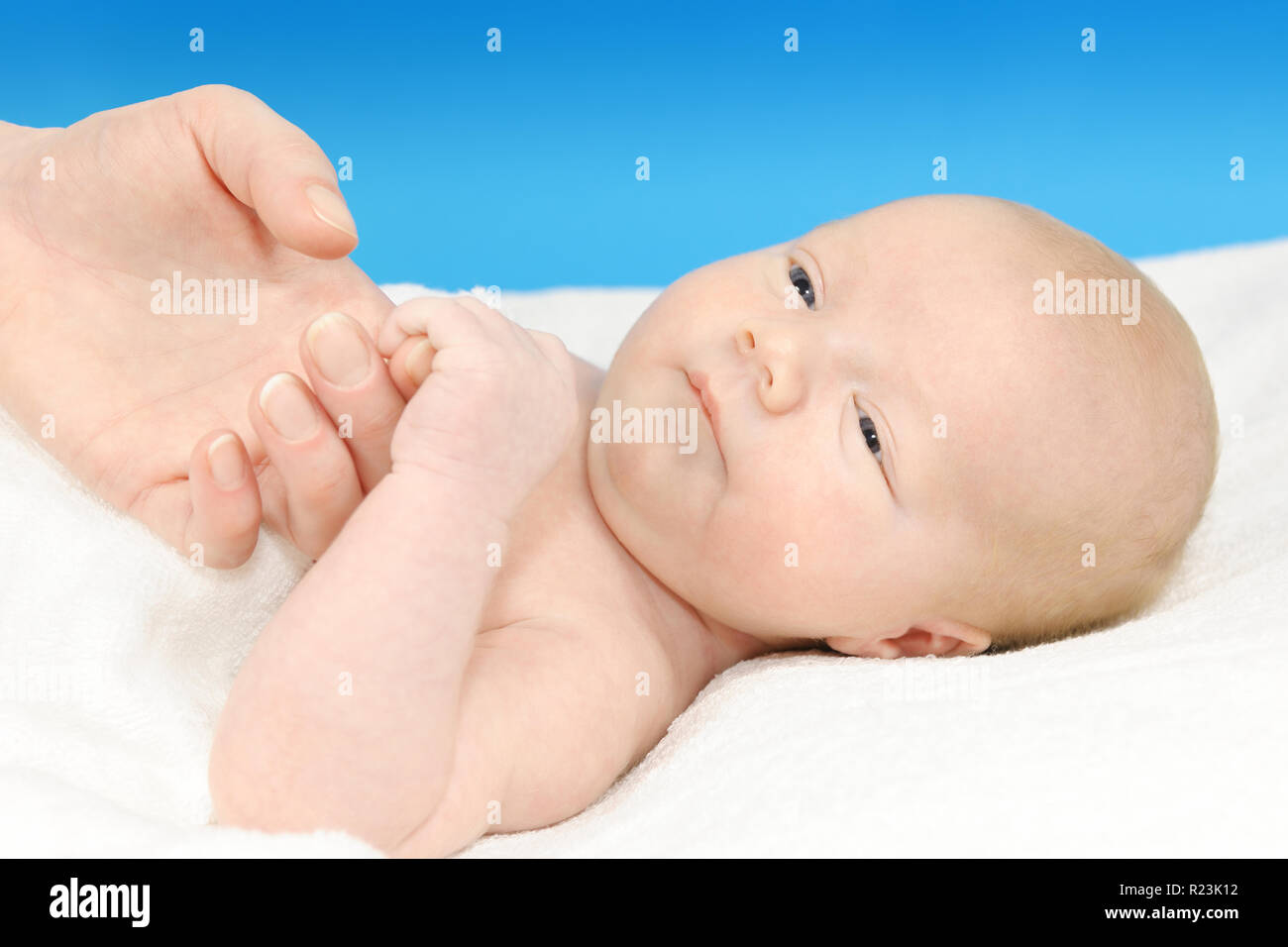Cute newborn, baby boy lying on a white blanket and his mother's hand Stock Photo