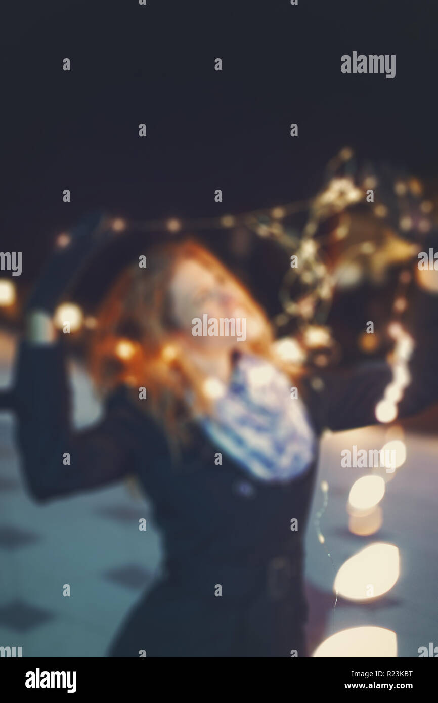 Young woman playing with christmas fairy lights at night, blurred template, outdoors in city Stock Photo