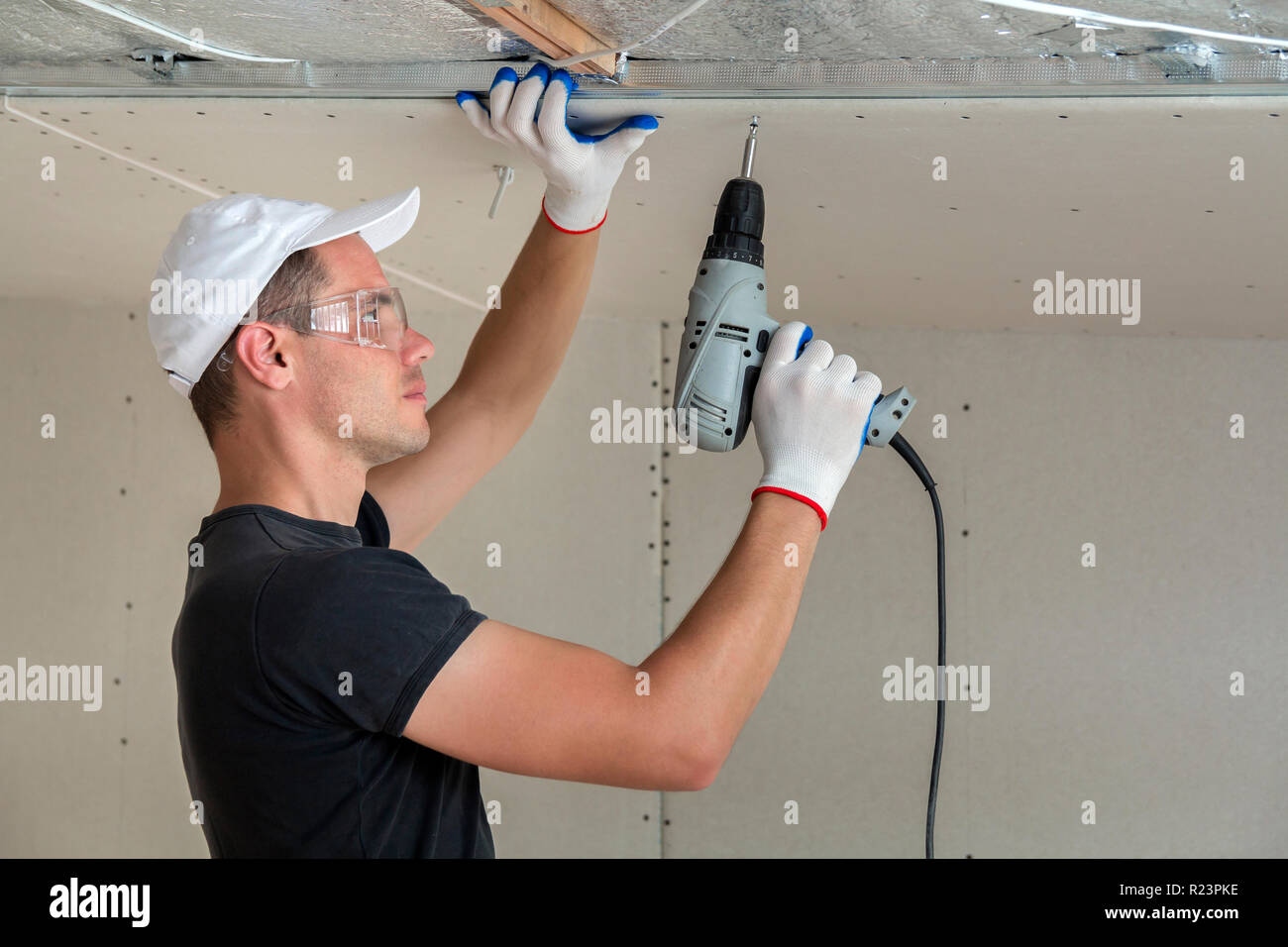 Young Man In Goggles Fixing Drywall Suspended Ceiling To Metal