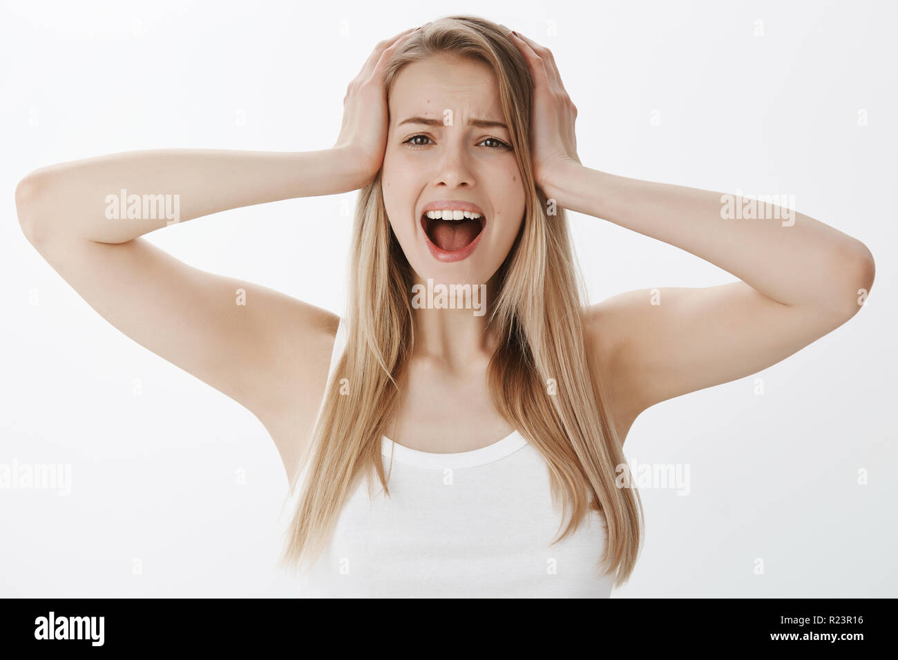 Girl panicking screaming, losing temper holding hands on head from overthinking, looking worried and depressed standing over gray background, yelling  Stock Photo