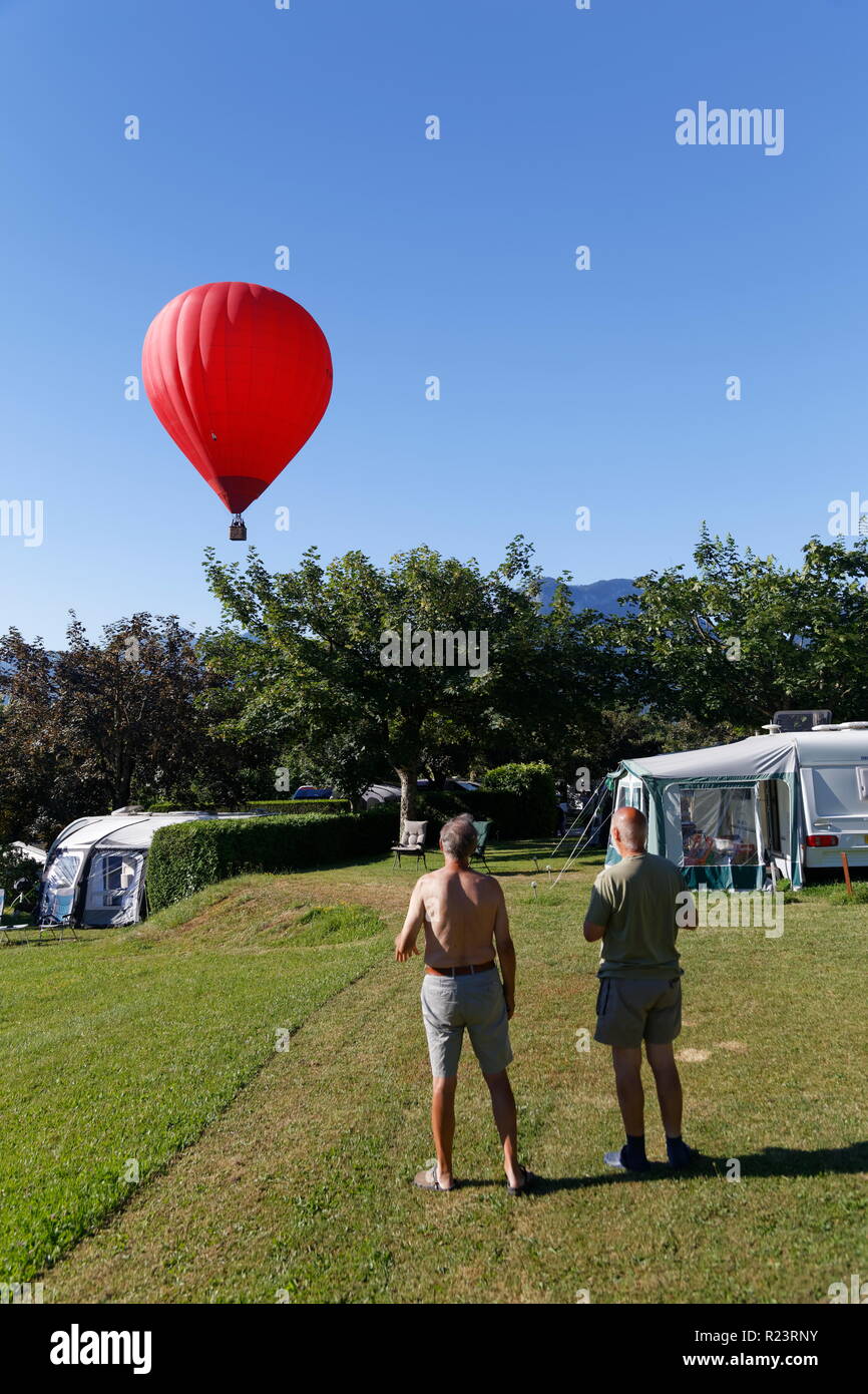 Holiday makers on a campsite watching a red balloon on an early morning flight over Lake Annecy France Stock Photo