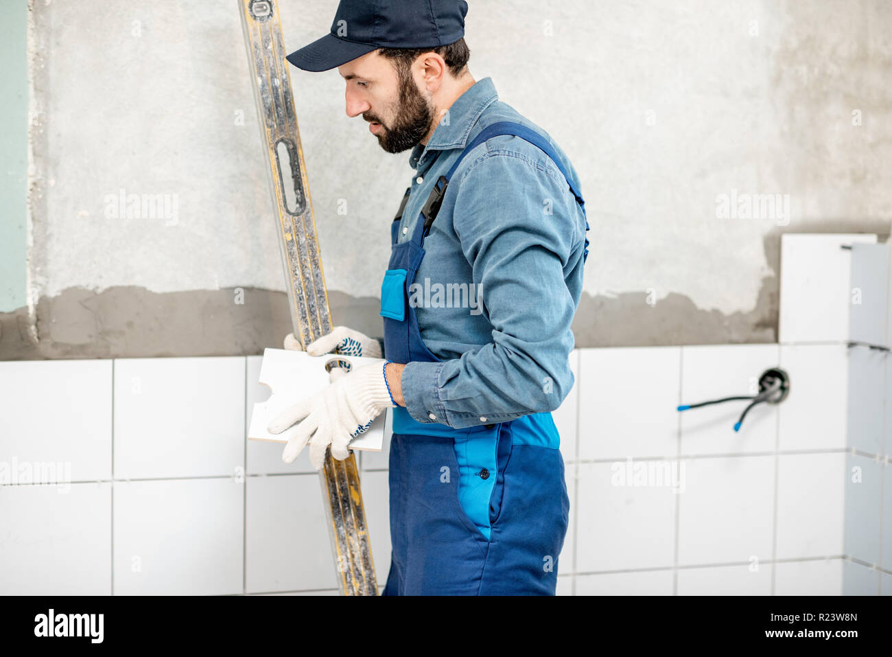Workman in blue uniform installing white ceramic tiles at the bathroom Stock Photo
