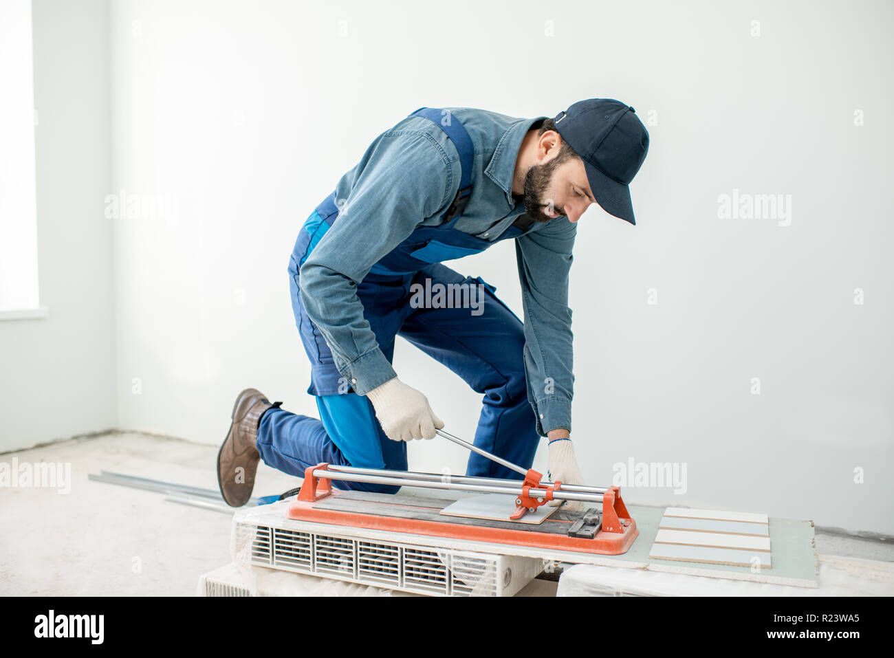 Workman cutting ceramic tiles with handy machine at the construction site indoors Stock Photo
