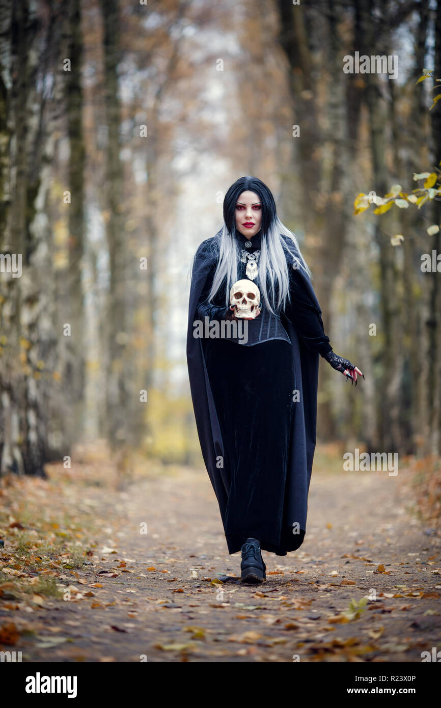 Portrait of witch girl in full growth in black cloak with skull Stock Photo  - Alamy