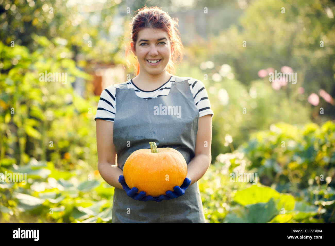 Photo of smiling girl with pumpkin in hands at garden Stock Photo