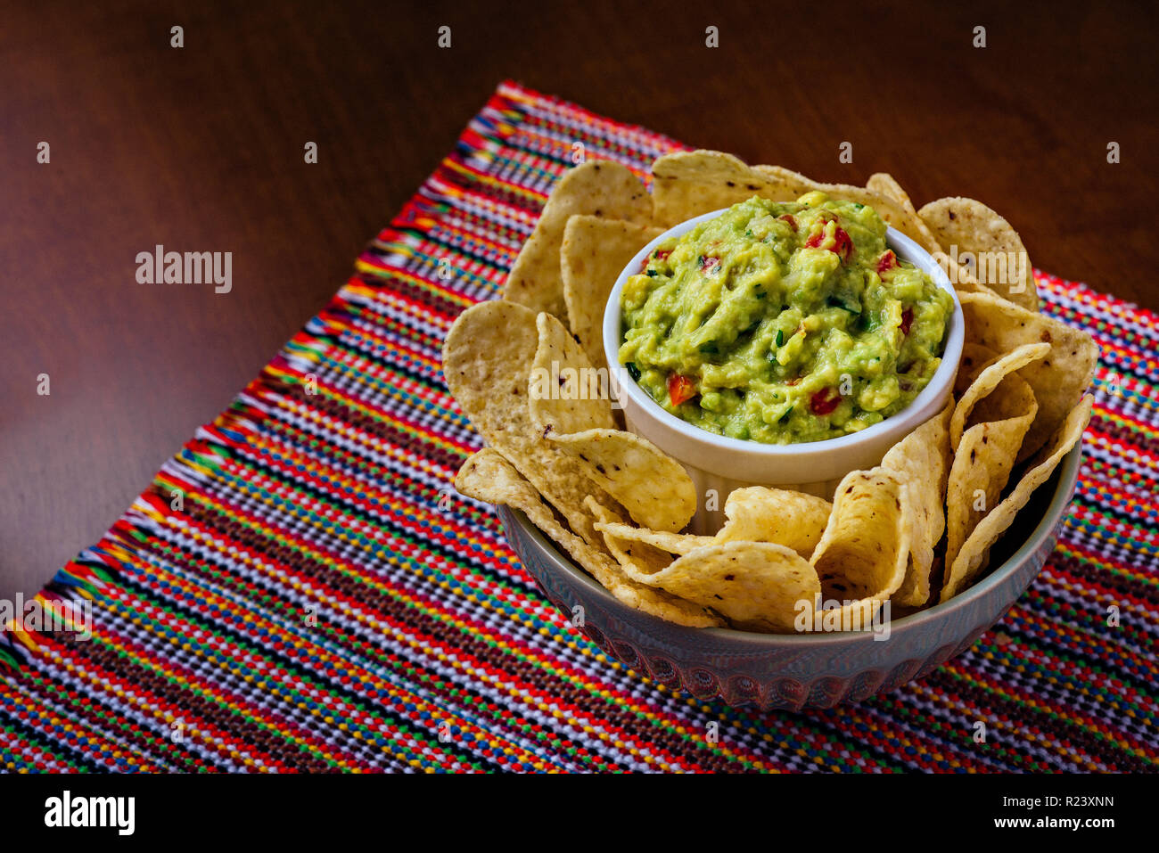 Corn nacho chips and avocado guacamole dipping sauce in a bowl over a table Stock Photo
