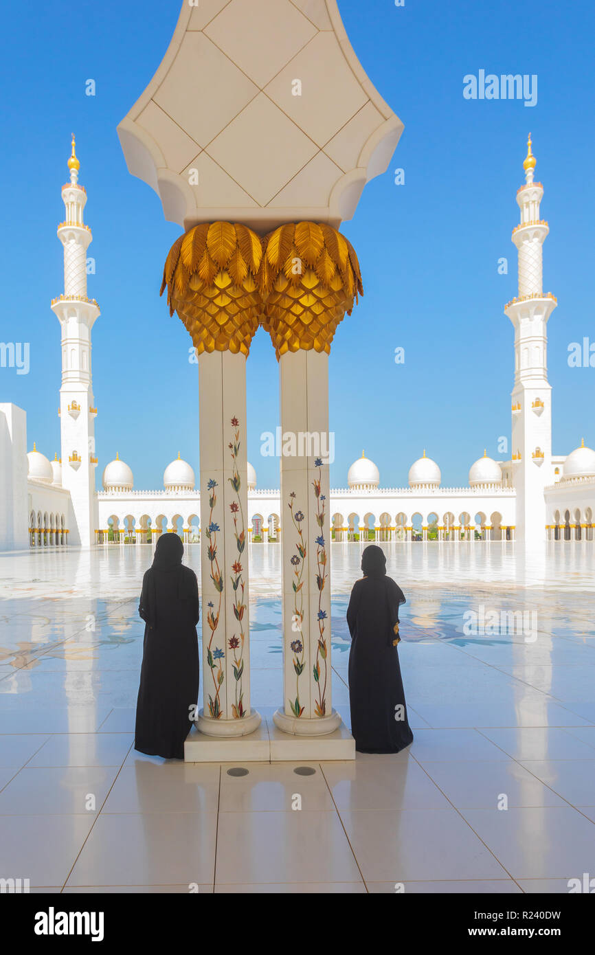 2 (two) tourist women wearing traditional black Abaya clothing admiring the beauty of Sheikh Zayed Grand Mosque in Abu Dhabi, United Arab Emirates. Stock Photo