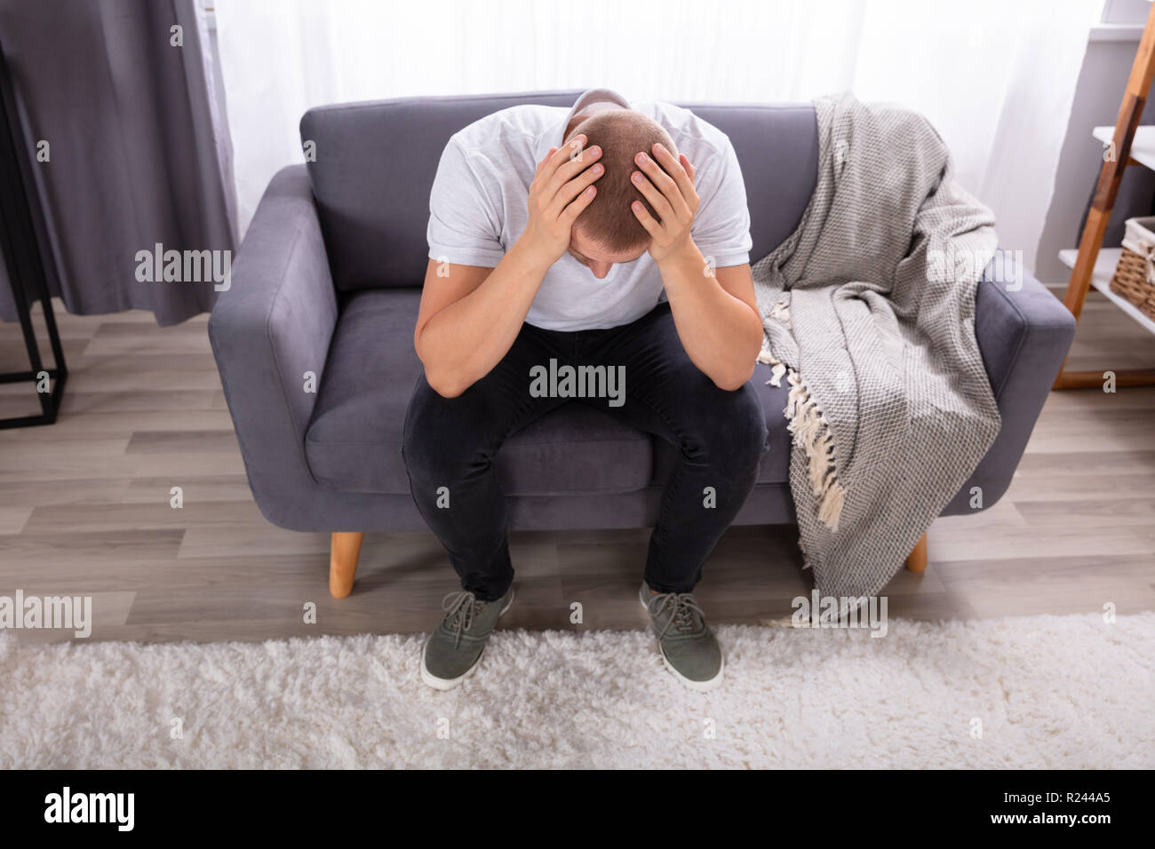 Young Man Sitting On Sofa Suffering From Headache Stock Photo
