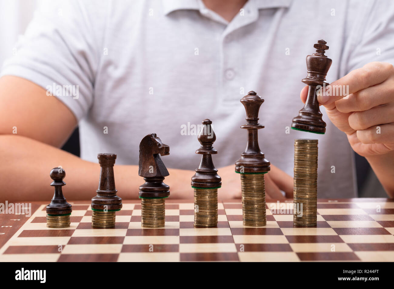 Man's Hand Placing King Chess Piece On Stacked Coins Over Chessboard Stock Photo