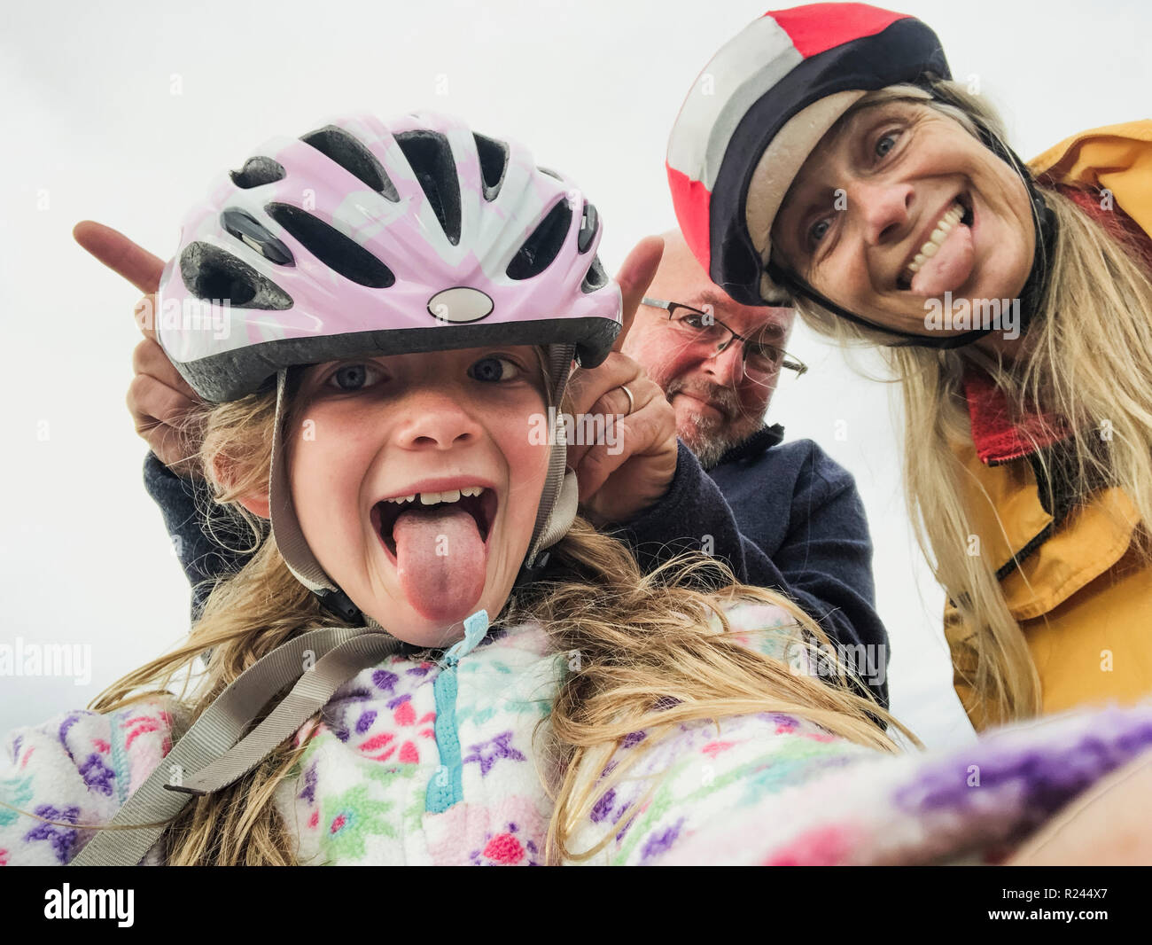 A close-up selfie of a happy family with one child, they are on an outdoor bikeride and pulling silly faces. Stock Photo
