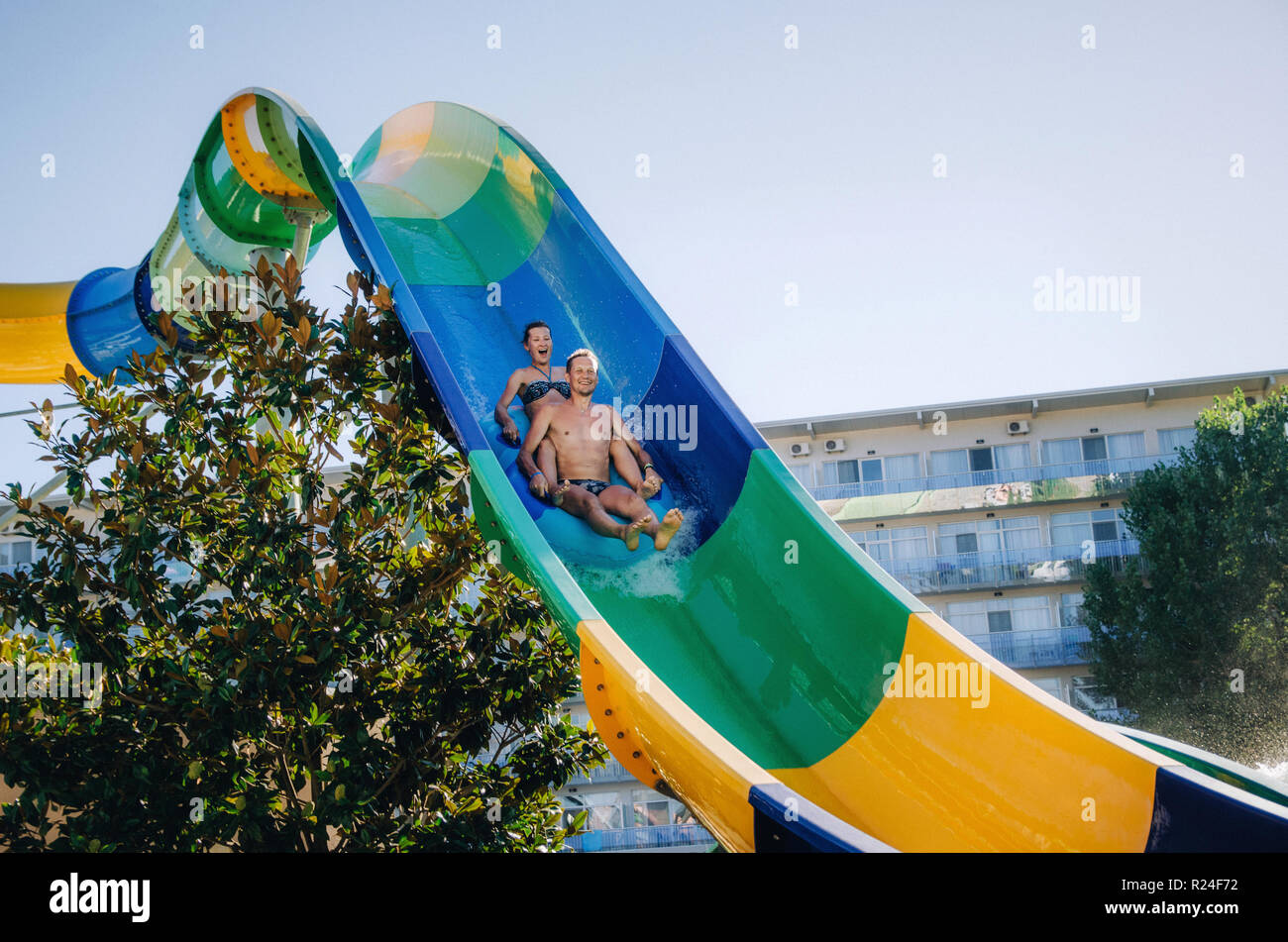 Funny couple taking a fast water ride on a float splashing water. Summer vacation with water park concept. Stock Photo