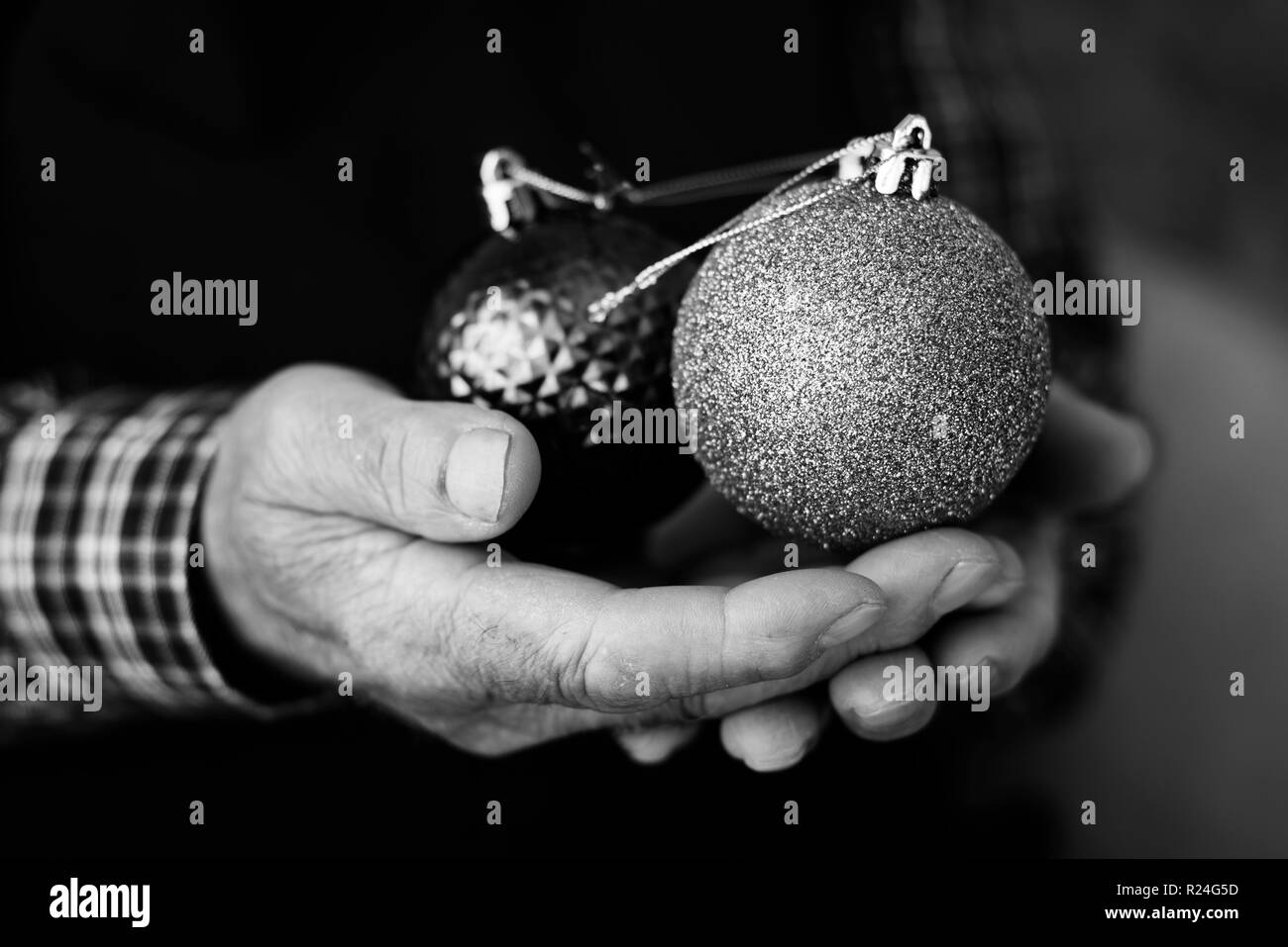 closeup of an old caucasian man with some christmas balls in his hands, in black and white Stock Photo