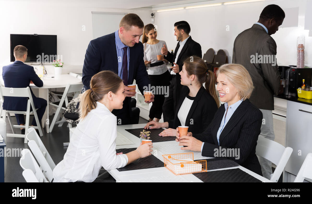 Cheerful multinational work team having break at office, drinking coffee and talking Stock Photo