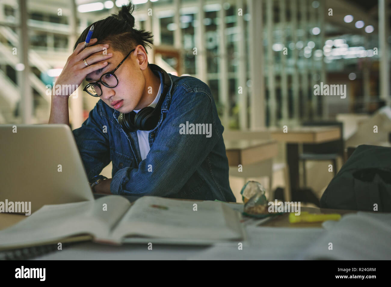 Male student sitting at library looking at laptop with hand on forehead. Depressed student sitting in library with laptop in college. Stock Photo
