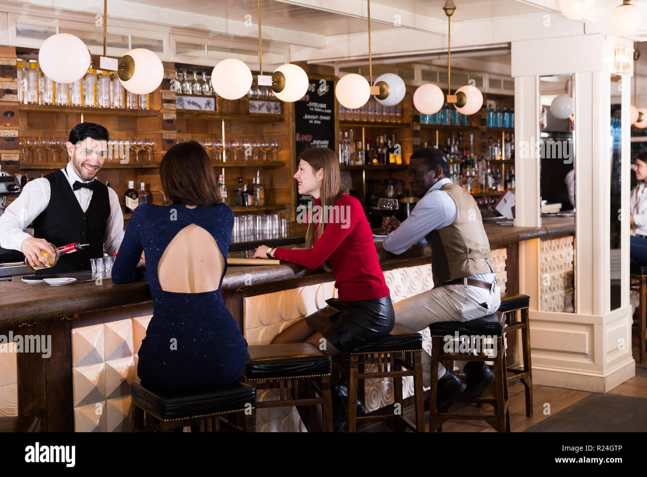 Young people sitting on bar in restaurant, ordering drinks to smiling
