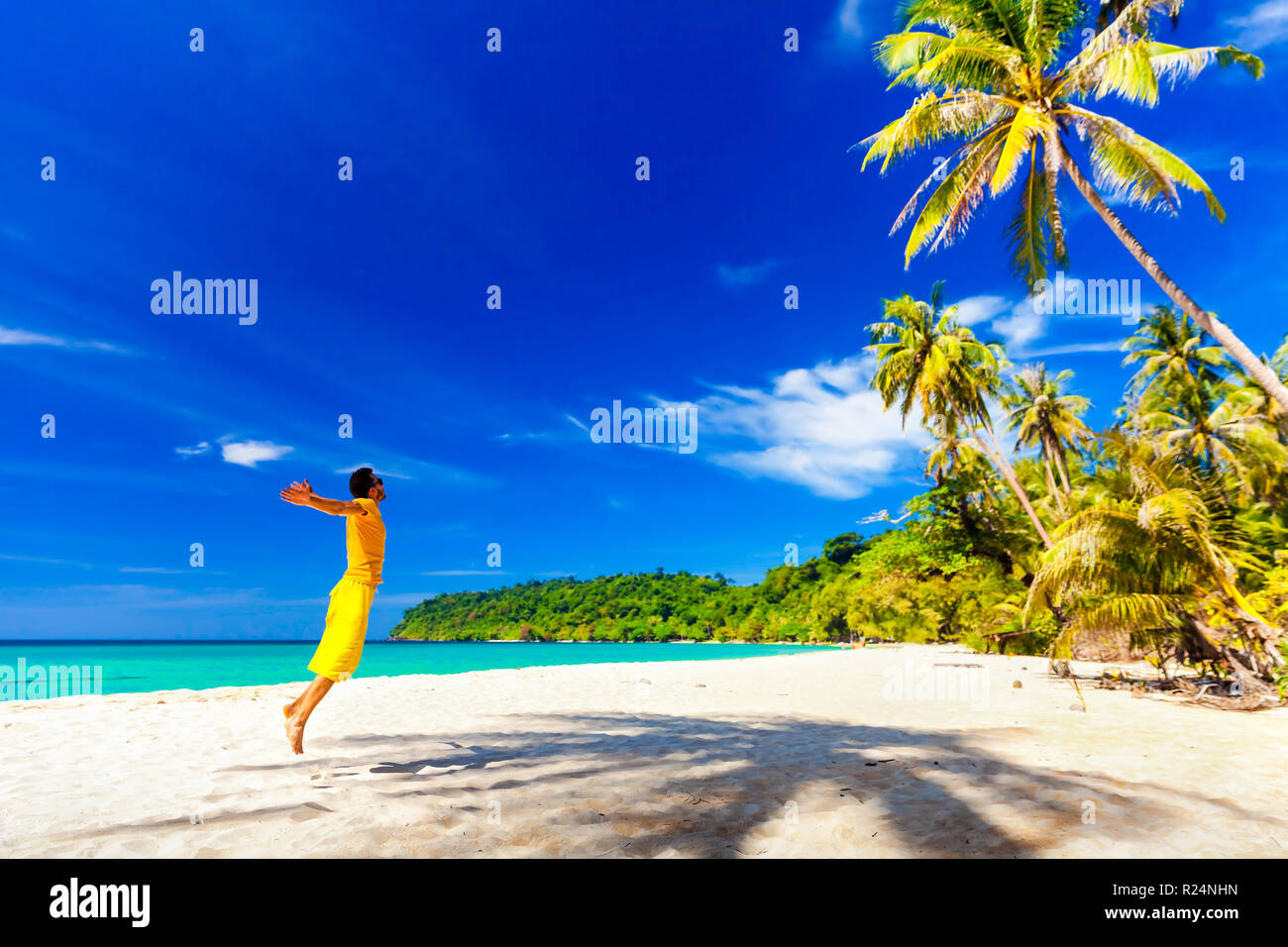 Active lifestyle and travel concept: Excited traveler man enjoy vacation on on tropical beach and jumping enjoying freedom Stock Photo