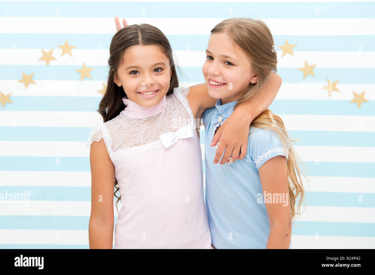 Girls children best friends hugs. Happy childhood concept. Kids schoolgirls preteens happy together. Friendship from childhood. Girls smiling happy faces hug each other while stand striped background. Stock Photo