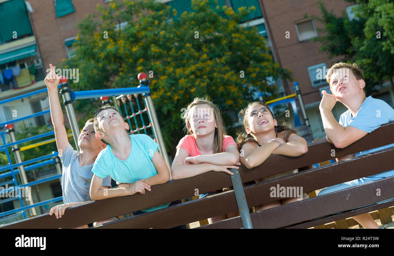 Five children sitting on a bench at the playground and point to ...