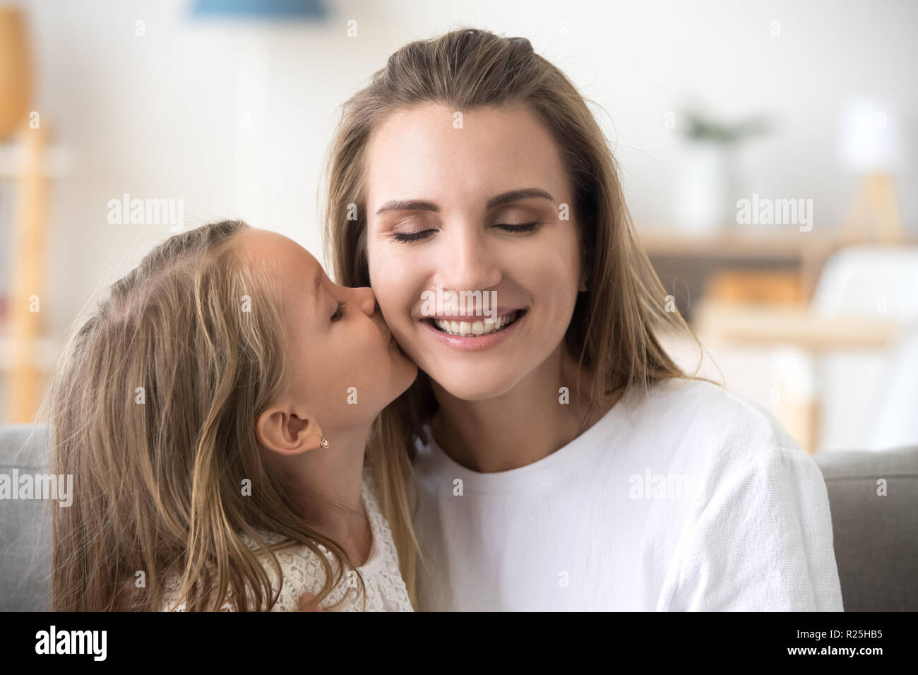 Cute little kid daughter kissing happy smiling mom on cheek Stock Photo