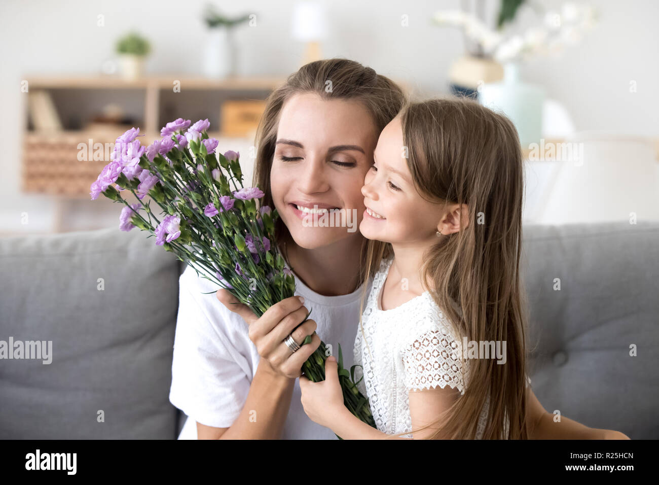 Smiling kid daughter giving flowers congratulating mom with moth Stock Photo