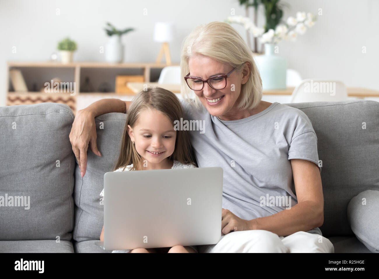 Smiling grandma and cute kid granddaughter watching cartoons on  Stock Photo