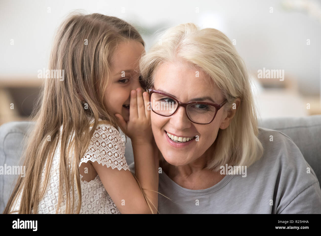 Cute little granddaughter whispering in ear telling secret to gr Stock Photo