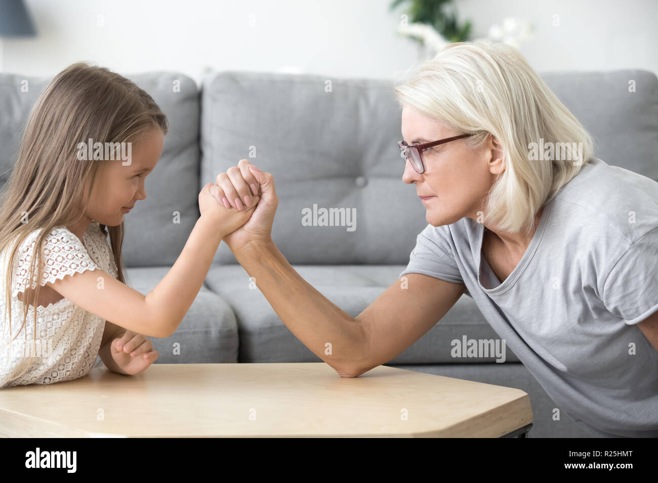 Old grandma and little granddaughter arm wrestling playing toget Stock Photo