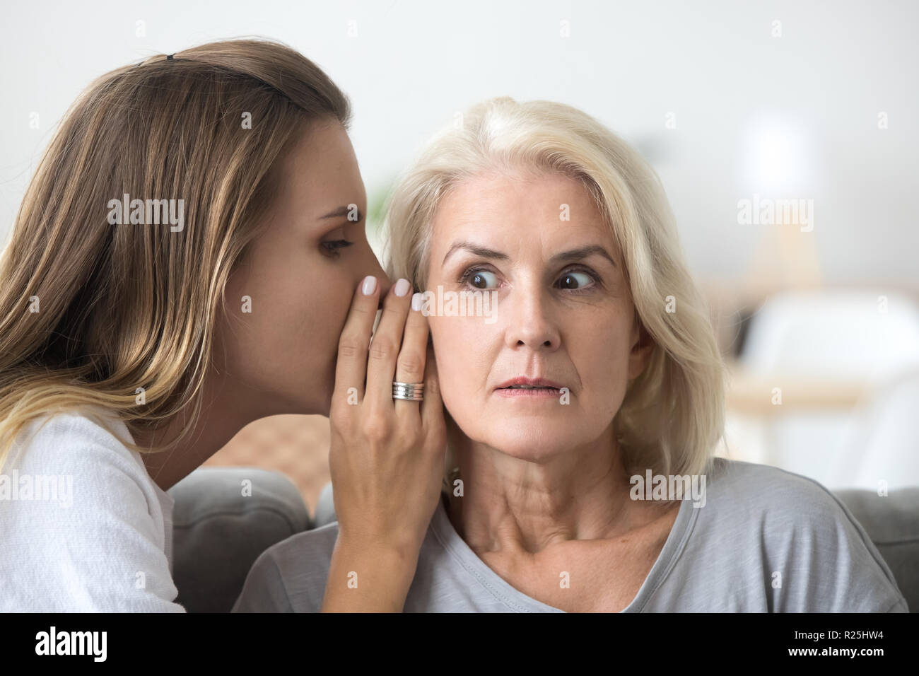 Shocked older woman listening to young friend whispering secret Stock Photo