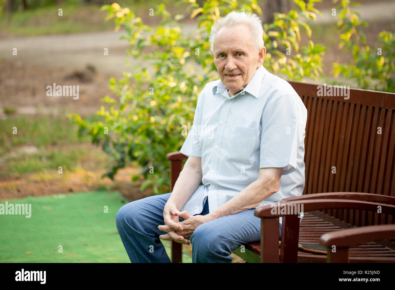 Older man sitting alone on a bench outdoors looking relaxed and smiling ...