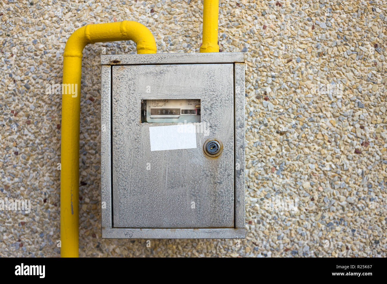 Close-up of metal steel gas meter box with connecting yellow pipes hanging on exterior light stone house wall. Construction, renovation, measurement t Stock Photo