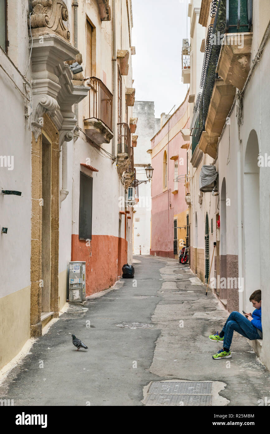 Young boy busy with his smart phone at Via San Luigi in historic center of Gallipoli, Apulia, Italy Stock Photo