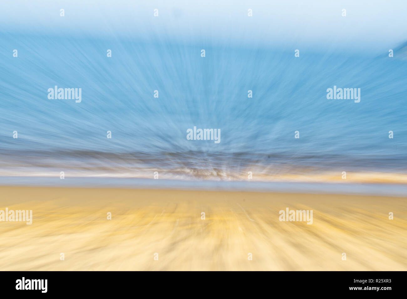 Coastal abstract golden sand blue water and pale sky in zoom blur for backgrounds Stock Photo