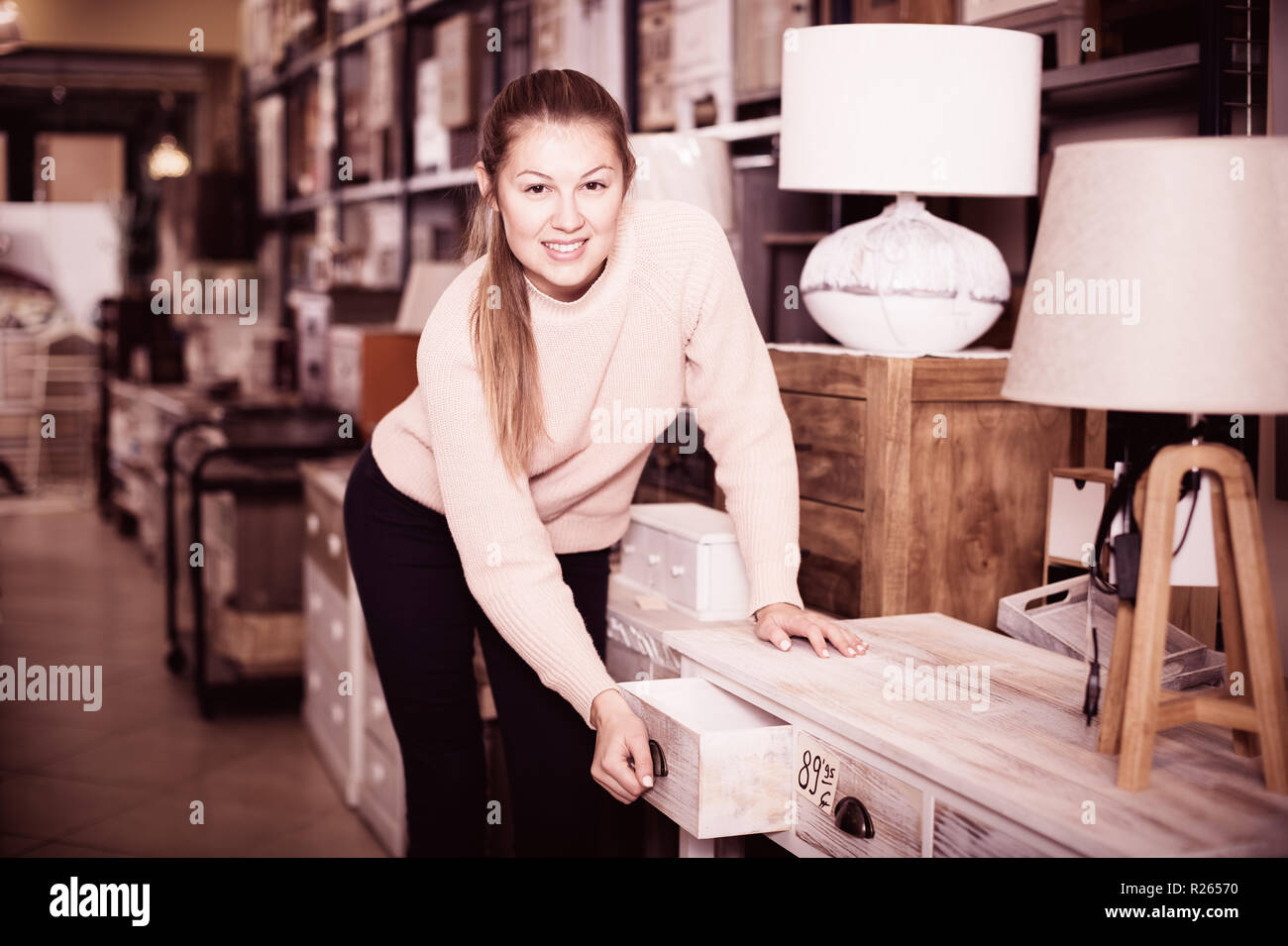 Positive woman customer touching table with drawers in furniture store