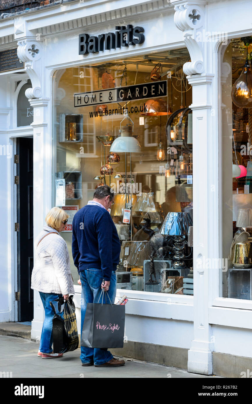 Mature couple standing outside Barnitt's home & garden shop, window shopping & viewing lamps in lighting display - York, North Yorkshire, England, UK. Stock Photo