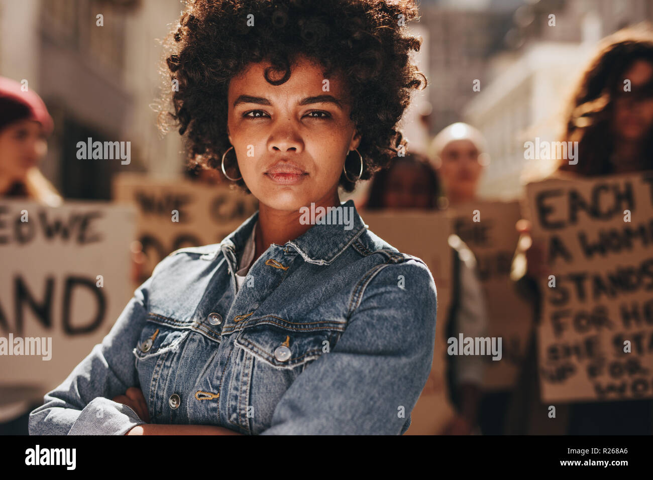 Young black woman with group of demonstrator in background outdoors. African woman protesting with group of activists outdoors on road. Stock Photo
