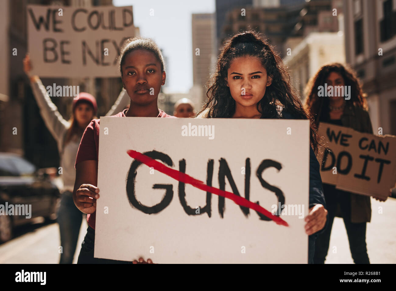 Two girls holding a banner with word guns strikethrough. Women holding sign that says not guns at a rally. Stock Photo