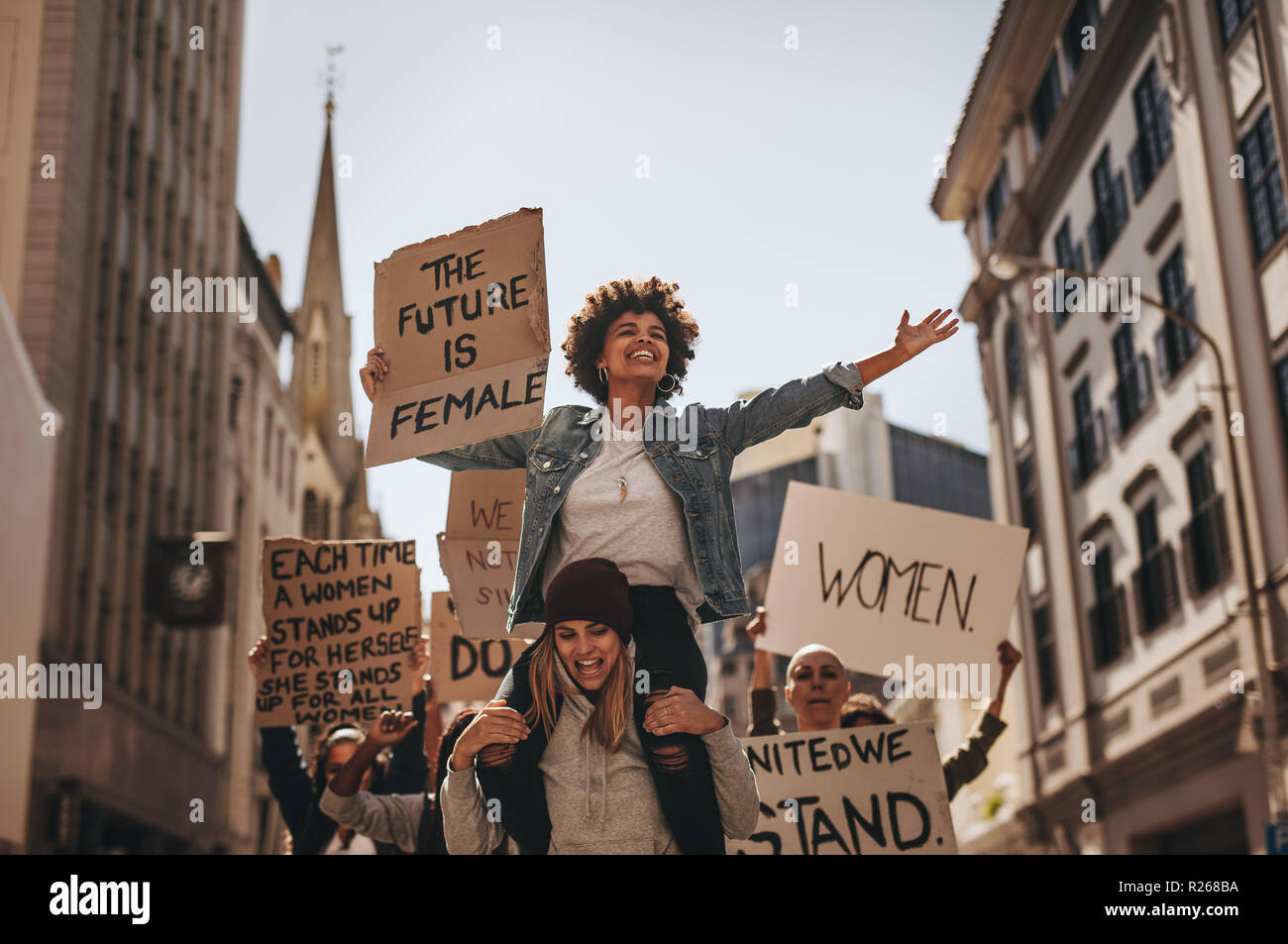 Group of female protesters marching on the road with signboards and smiling. Women holding protest banners and marching outdoors. Stock Photo