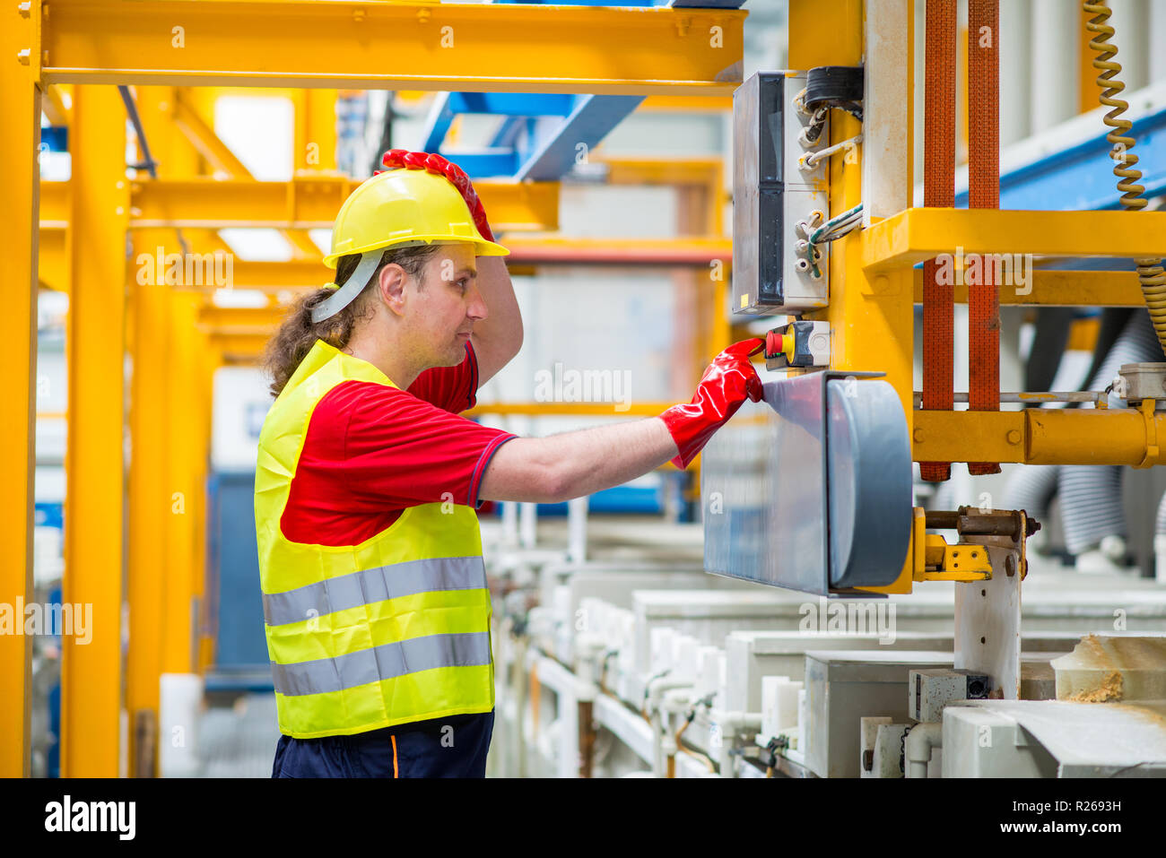 Worker in a factory operating a factory machine pressing a red button. Stock Photo