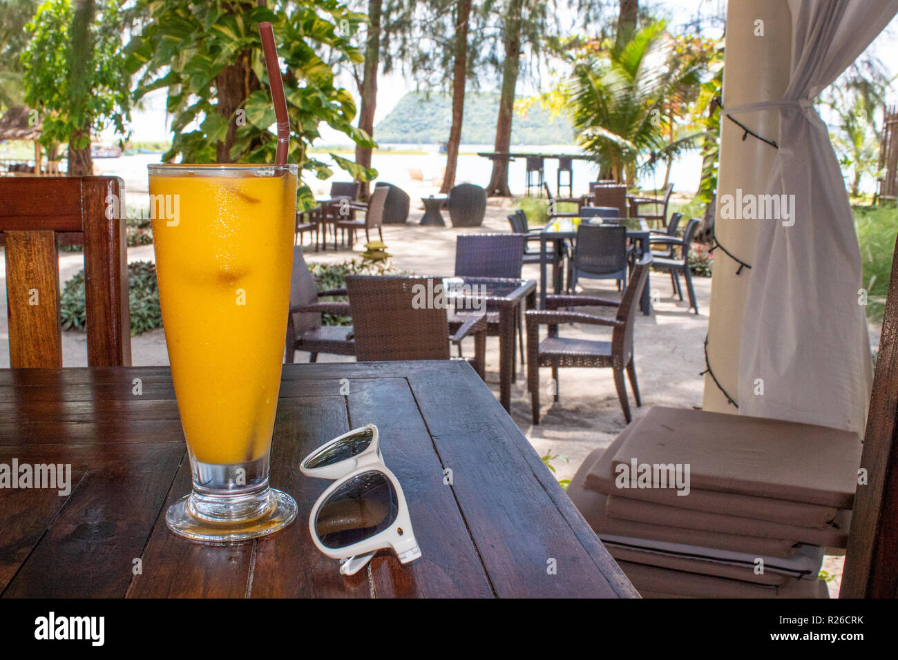 Orange or mango juice next to sunglasses standing on table in beach bar