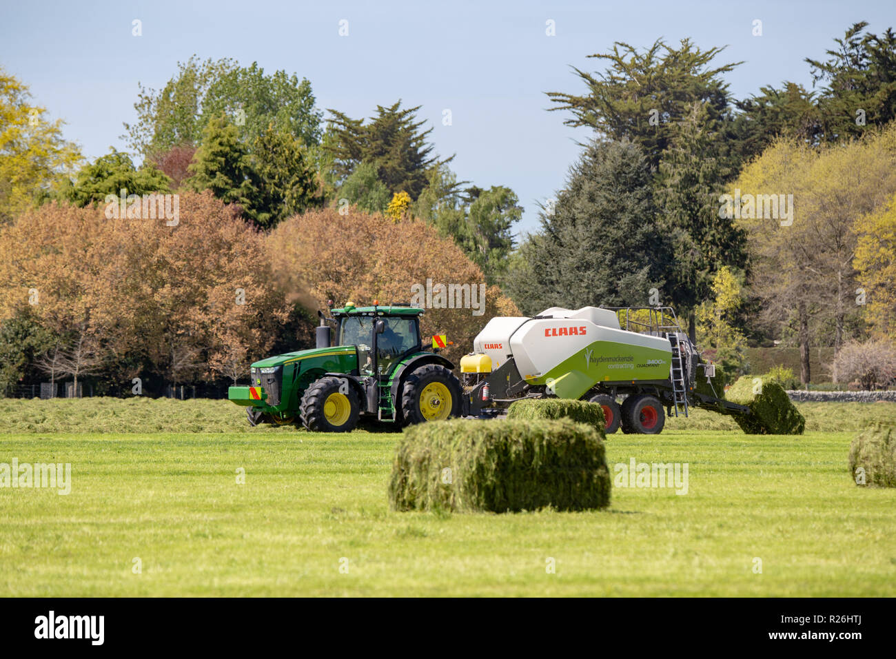 Geraldine, Canterbury, New Zealand - October 21 2018: A farming scene with a John Deere tractor and a Claas baler making hay bales in spring Stock Photo